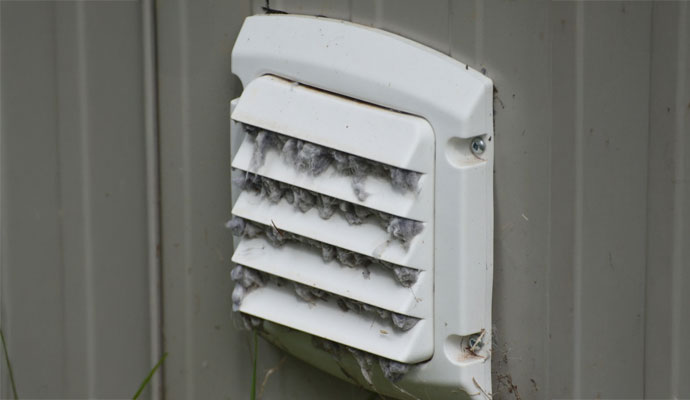 Exterior white dryer vent cover severely clogged with visible gray lint buildup between the slats