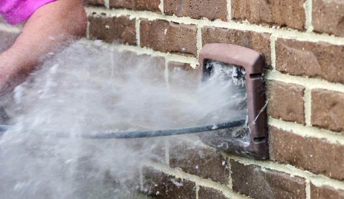 Large amount of white lint being blown out of an exterior dryer vent on a brick wall