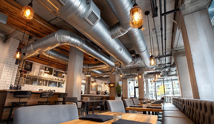 Large industrial silver metal air ducts running along the ceiling of a modern restaurant