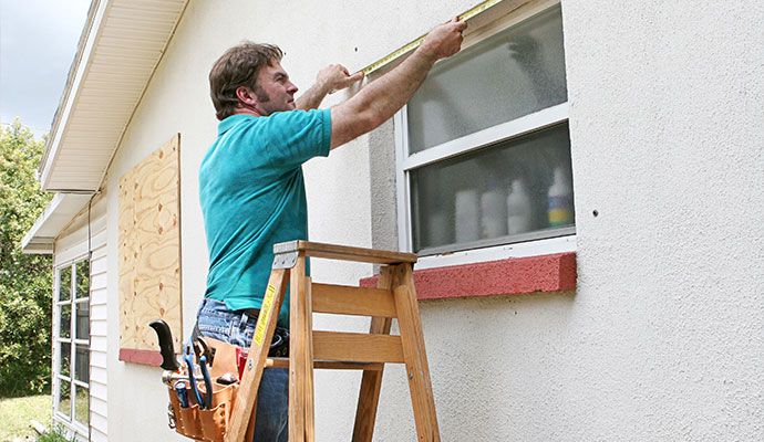 A professional standing on a wooden ladder measuring a window for emergency board-up assistance