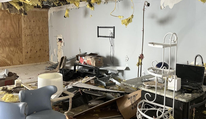 Room with damaged walls ceiling insulation debris and broken furniture
