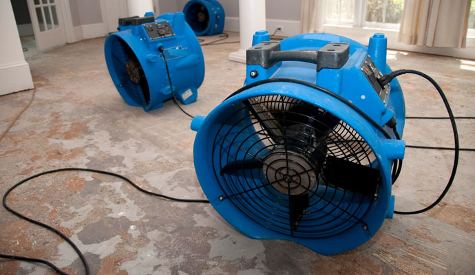 Blue industrial air mover fans drying a floor during water damage restoration service