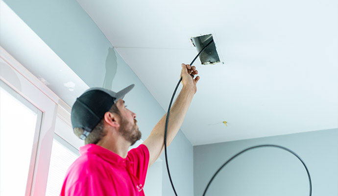 Technician inserting a cleaning tool into a ceiling air duct vent to remove dust and debris