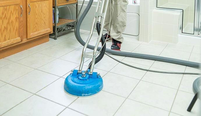 Technician cleaning white bathroom floor tiles with a professional floor cleaning machine