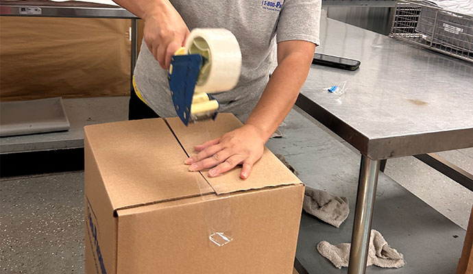 Worker sealing a cardboard moving box with packing tape